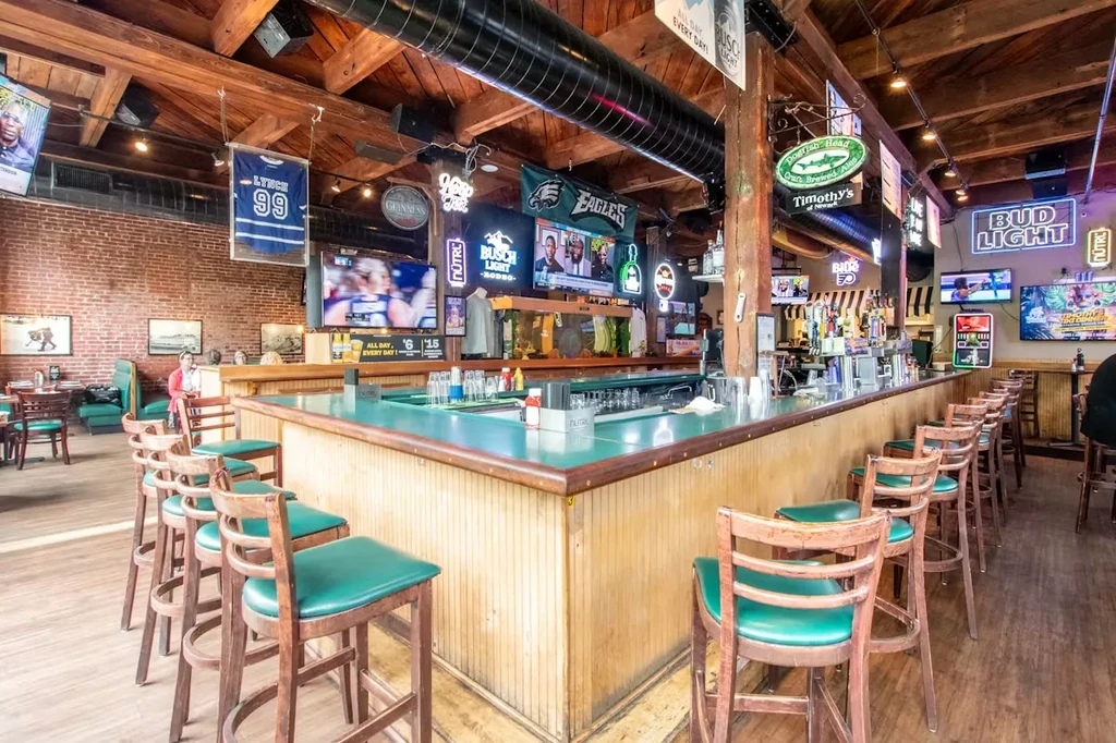 Bright sports bar with teal counter, suspended TVs, brick walls, beer signs.