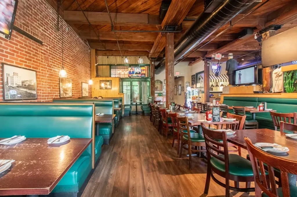 Empty rustic-industrial restaurant with teal booths, wooden tables, and TVs.
