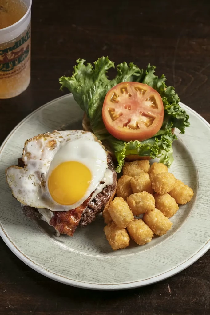 Open-faced burger with bacon, egg, tater tots, and beer.