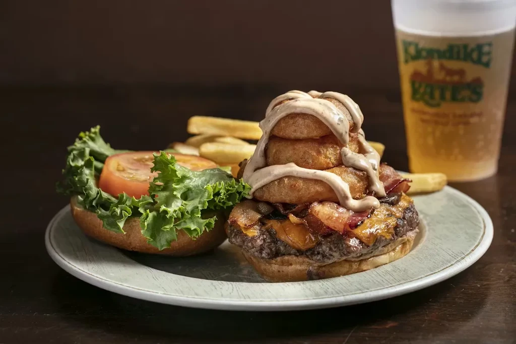 Elaborate burger with onion rings, fries, and Klondike Kate's beer.