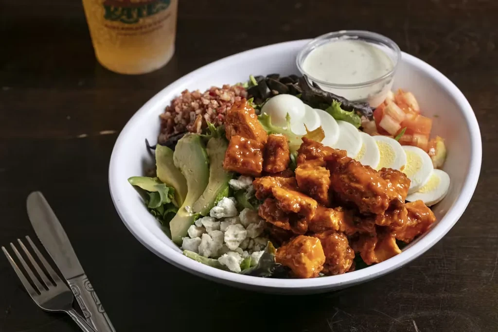 Buffalo chicken salad with avocado, cheese, eggs, and dressing, on table.