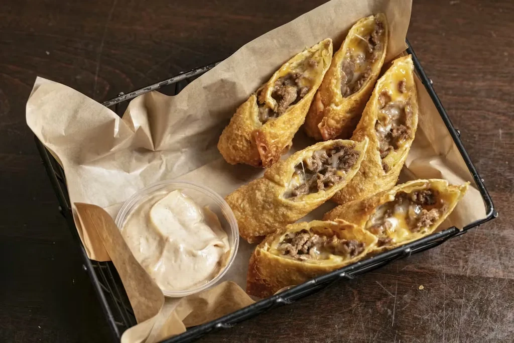 Halved, golden-fried egg rolls with savory filling and dipping sauce.