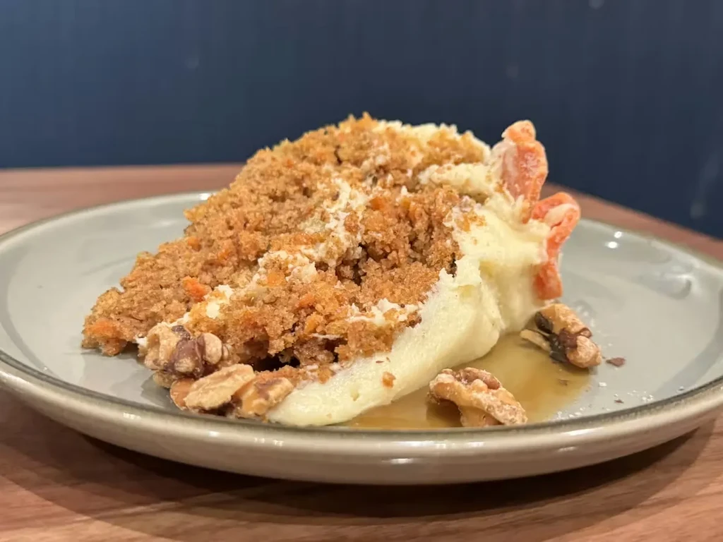Carrot cake slice with cream cheese frosting, walnuts, and caramel sauce.
