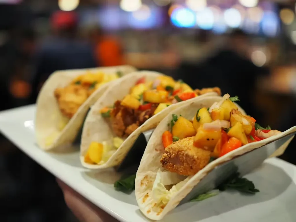 Three fried fish tacos with vibrant mango salsa and cilantro.