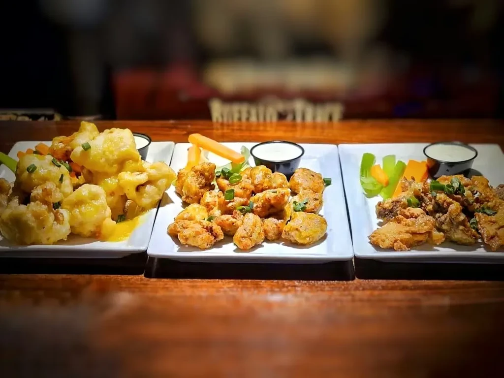 Three plates of assorted fried bites with vegetables and dipping sauces.