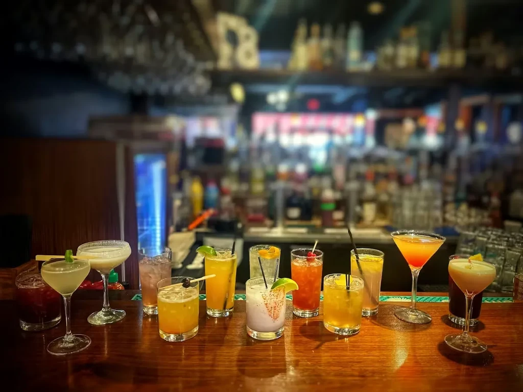 Eleven diverse colorful cocktails on a modern bar counter.