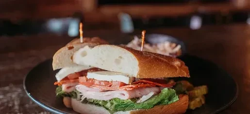 Layered gourmet sandwich with meat, cheese, lettuce, and side potatoes.