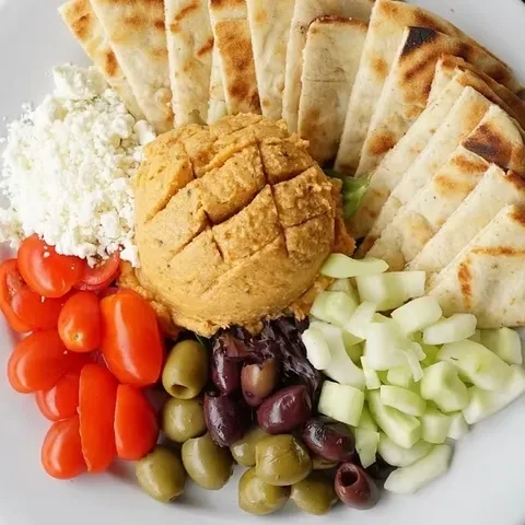 Platter with hummus, pita bread, feta, tomatoes, olives, and cucumbers.