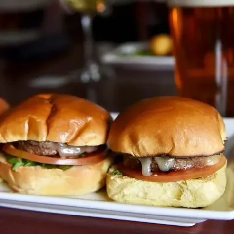 Two mini-burgers with melted cheese, vegetables, and restaurant background.