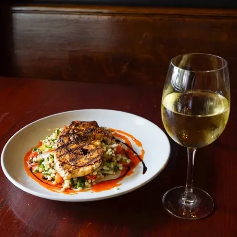 Grilled protein dish with grains, two sauces, and white wine.