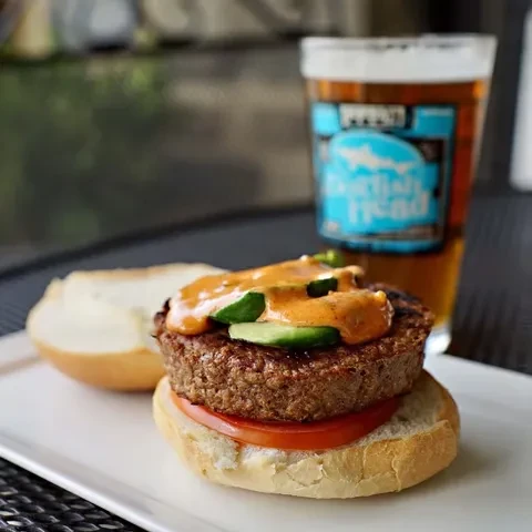 Open-faced burger with sauce and cucumber, Dogfish Head beer on patio.