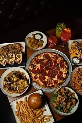 Overhead shot of a table laden with pizza, tacos, burger, nachos, drinks.
