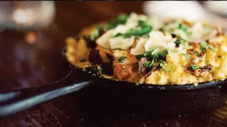Creamy mac and cheese in a black skillet with cheese and herbs.