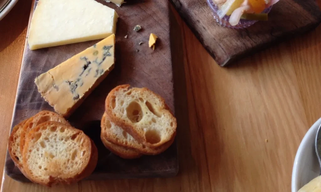 Overhead view of a wooden board with cheese, crackers, and relish.