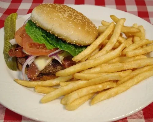 Classic loaded burger, golden fries, and pickle on a checkered tablecloth.