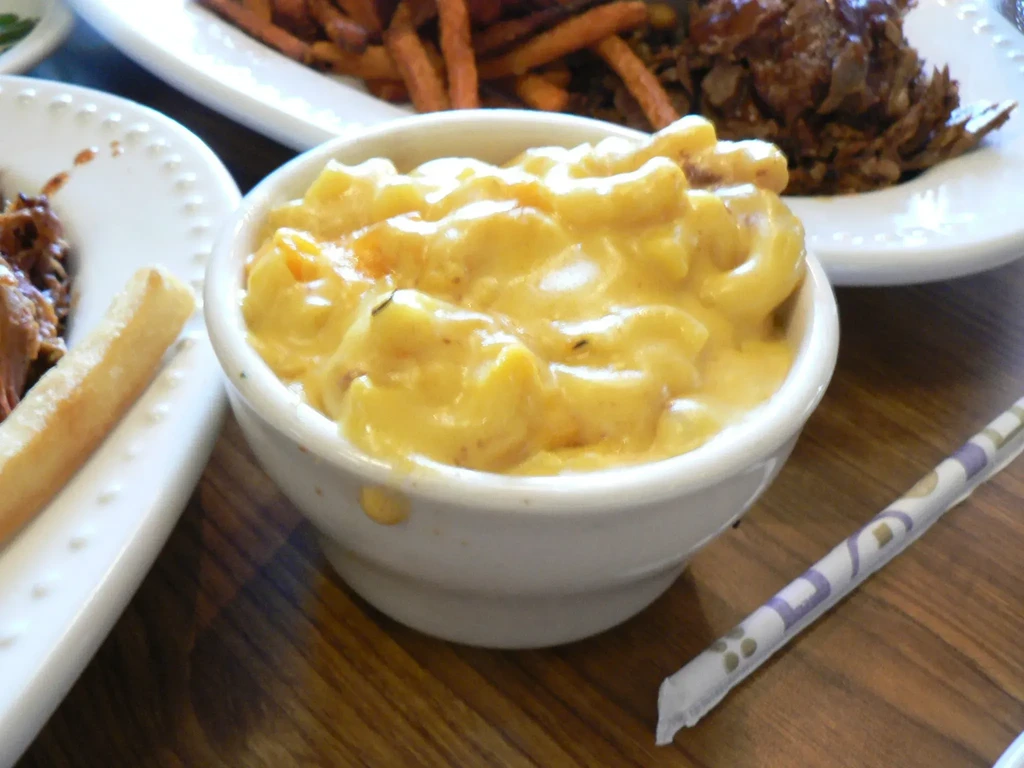 White bowl of creamy, golden macaroni and cheese on a wooden table.