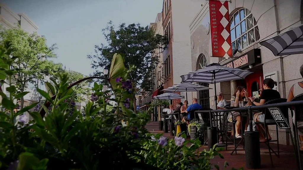 Chelsea Tavern outdoor dining with people, flowers, and striped umbrellas.