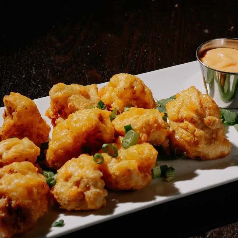 Golden-brown fried food garnished with green onions and orange dipping sauce.