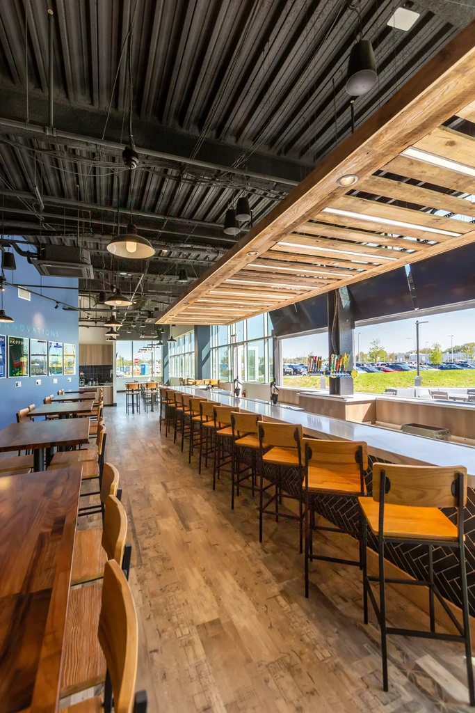 Contemporary restaurant interior with long bar, dining tables, and industrial ceiling.