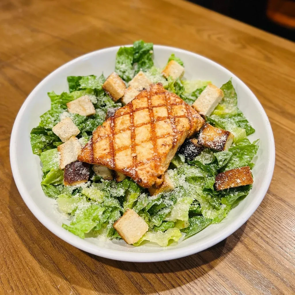 Close-up of a Caesar salad with grilled protein, croutons, and cheese.