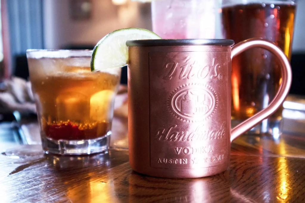 Tito's copper mug with lime, other drinks on a reflective table.