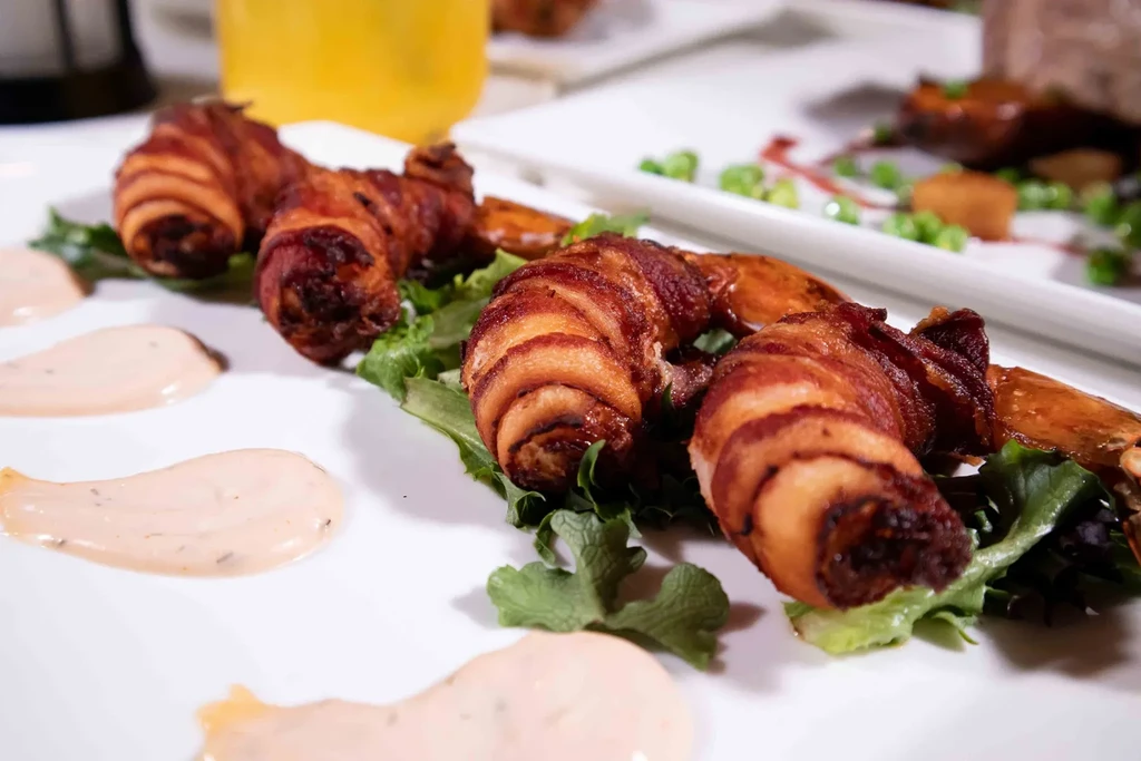 Crispy bacon-wrapped appetizers with creamy sauce on a white plate.
