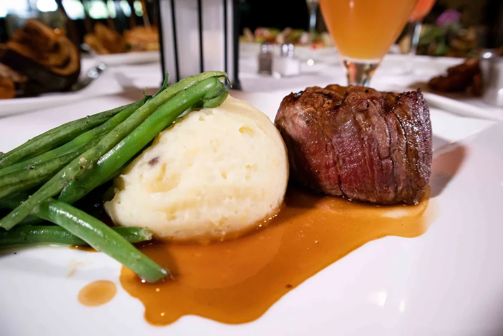 Plated steak, mashed potatoes, and green beans with gravy in a restaurant.