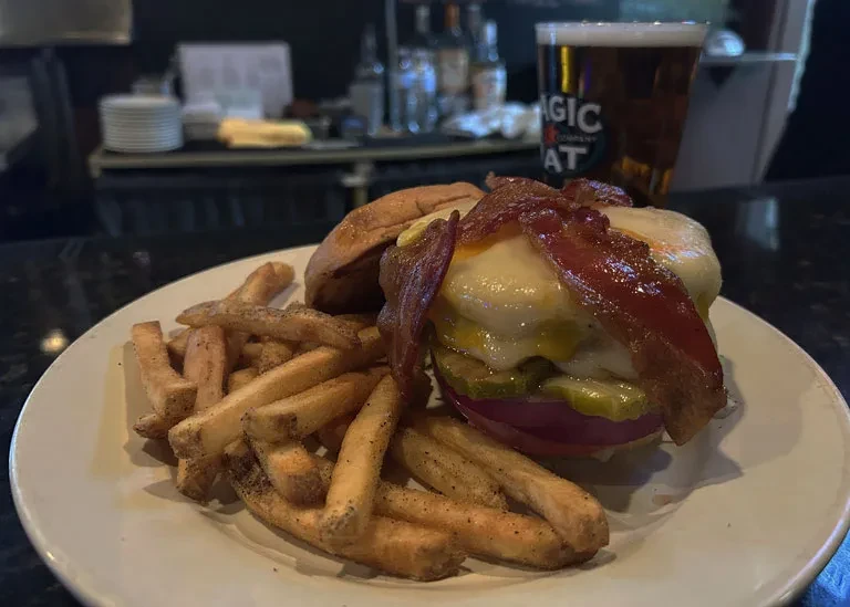 Burger with bacon, melted cheese, pickles, and seasoned golden fries.