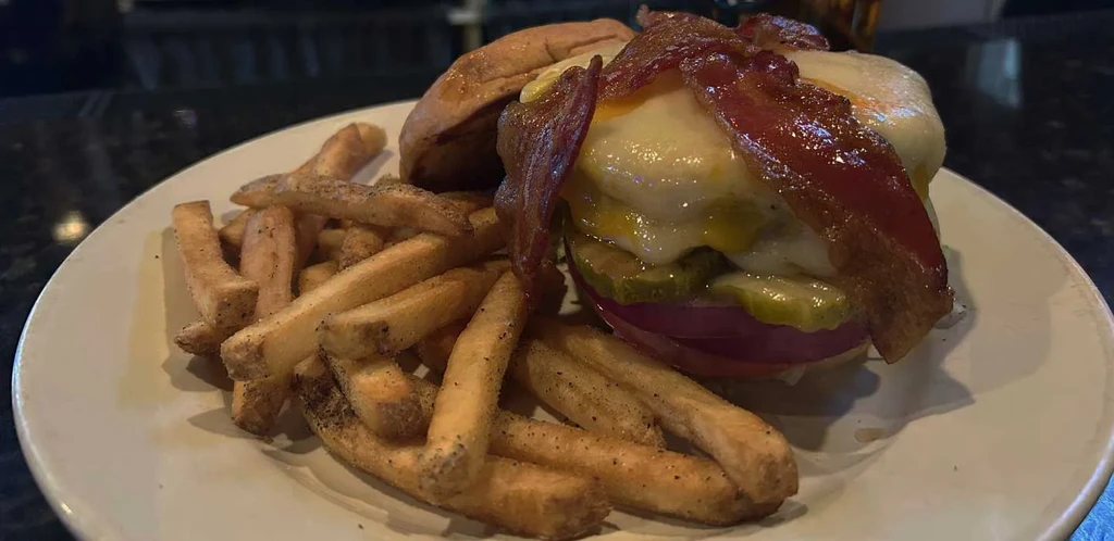 Burger with melted cheese, crispy bacon, pickles, and french fries.