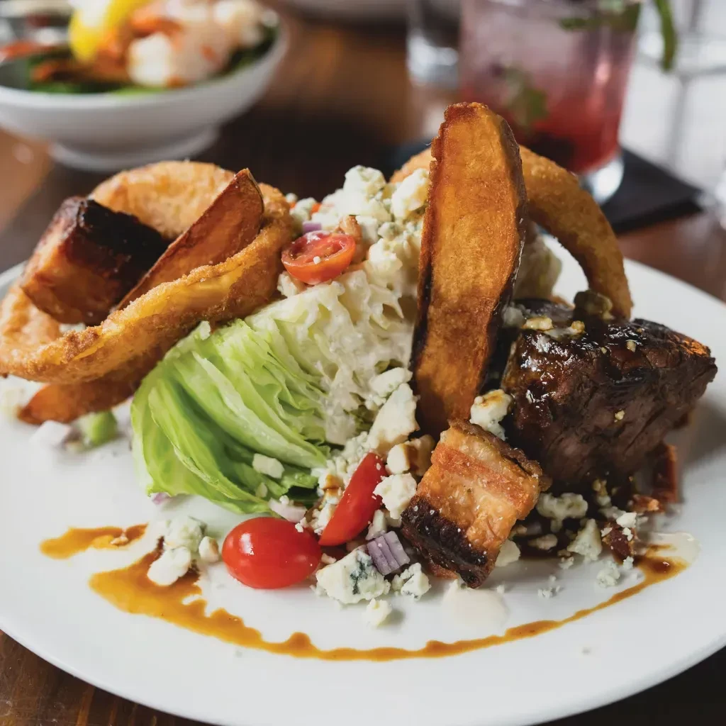 Plate with glazed meat, potato wedges, lettuce, blue cheese, and tomatoes.