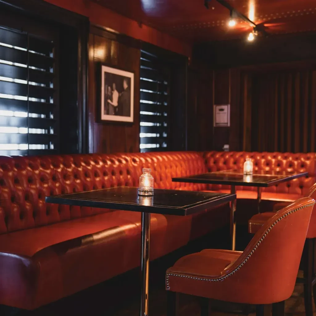 Dimly lit restaurant interior with a red tufted leather banquette.