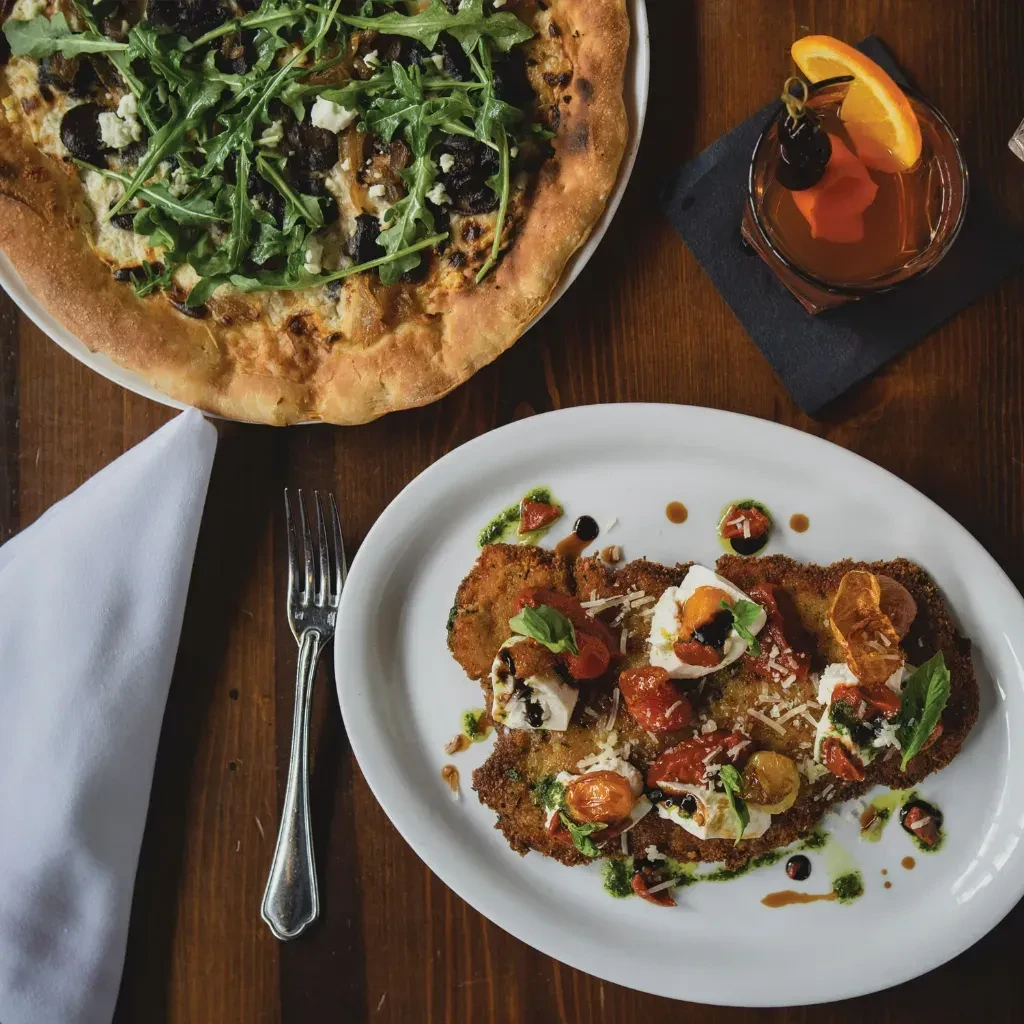 Flat lay of pizza, cocktail, and breaded schnitzel on wooden table.