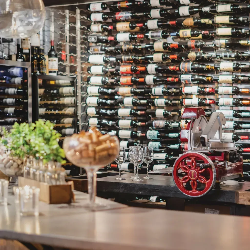 Bar counter with glasses, vintage red slicer, and wine storage.