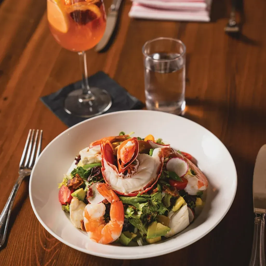 Seafood salad with lobster, shrimp, drinks, cutlery on table.
