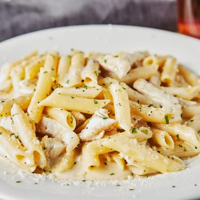 Penne pasta with creamy chicken sauce, garnished with herbs and cheese.