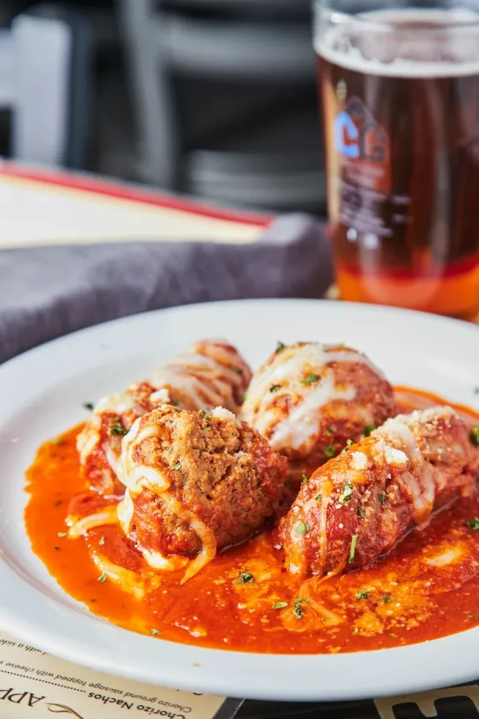 Meatballs with red sauce, melted cheese, herbs, at a restaurant.