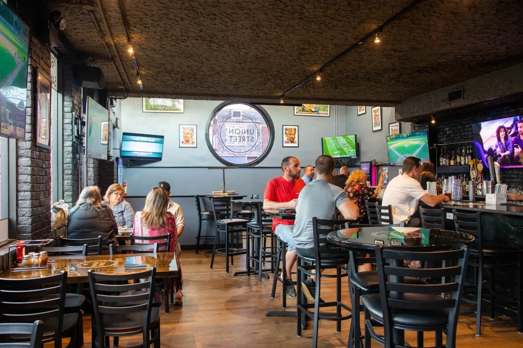 Bustling sports bar interior with TVs, dining areas, and a long bar.