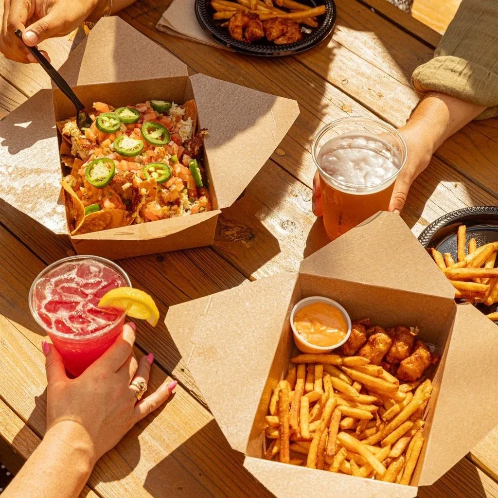 Top-down view of loaded nachos, fries, and drinks on a wooden table.