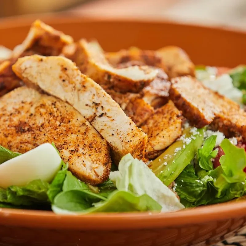 Grilled chicken salad with greens and cheese in a rustic bowl.