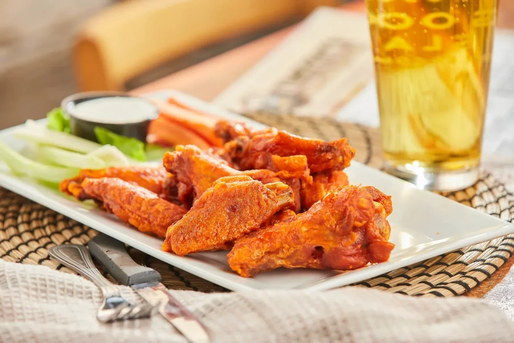 Platter of buffalo wings, celery, carrots, creamy dip, and beer.