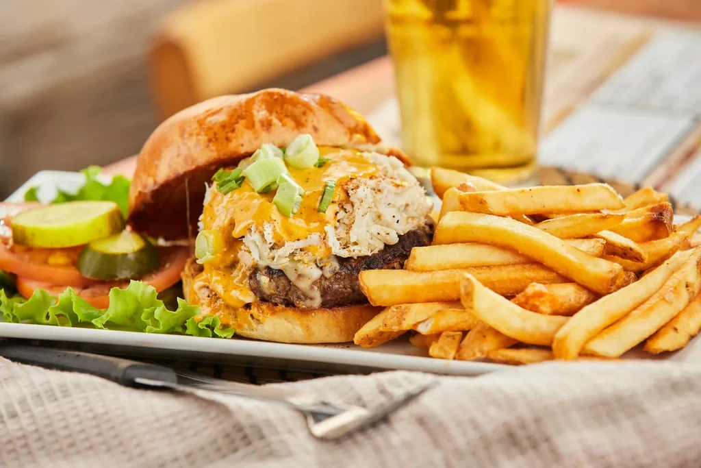 Gourmet burger with crab, cheese, sauce, fries, and side salad.