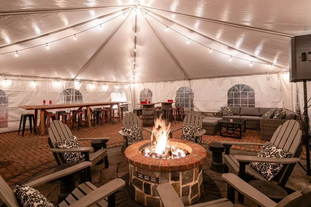 Large event tent with central fire pit and various seating areas.