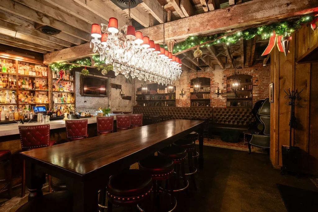 Rustic elegant bar with crystal chandelier, festive greenery, leather seating.