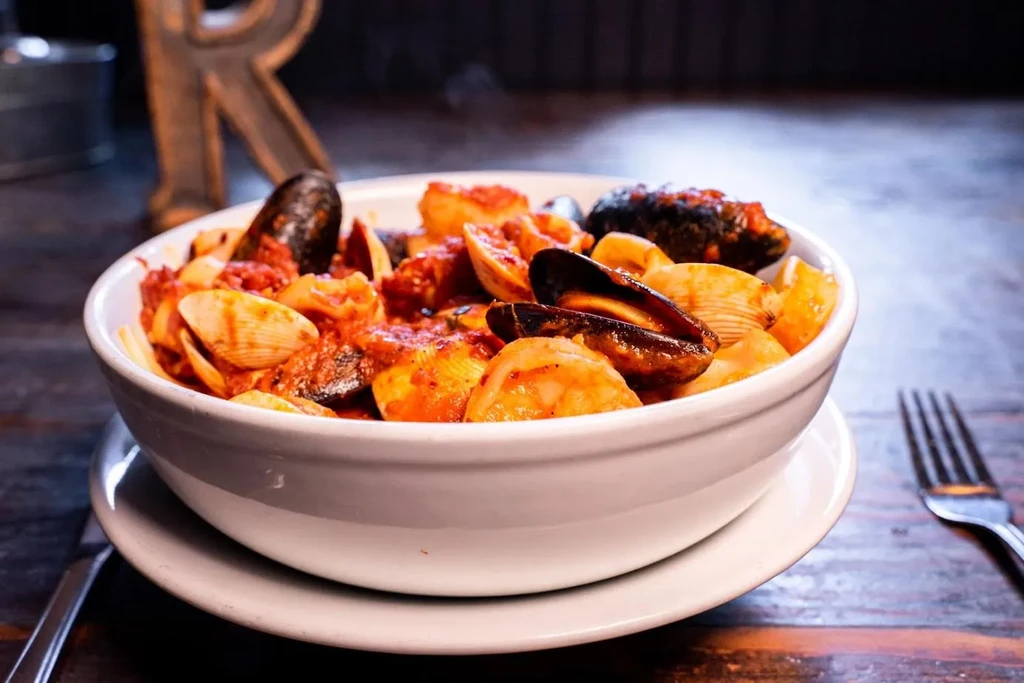 White bowl of shell pasta with mussels and clams in reddish sauce.