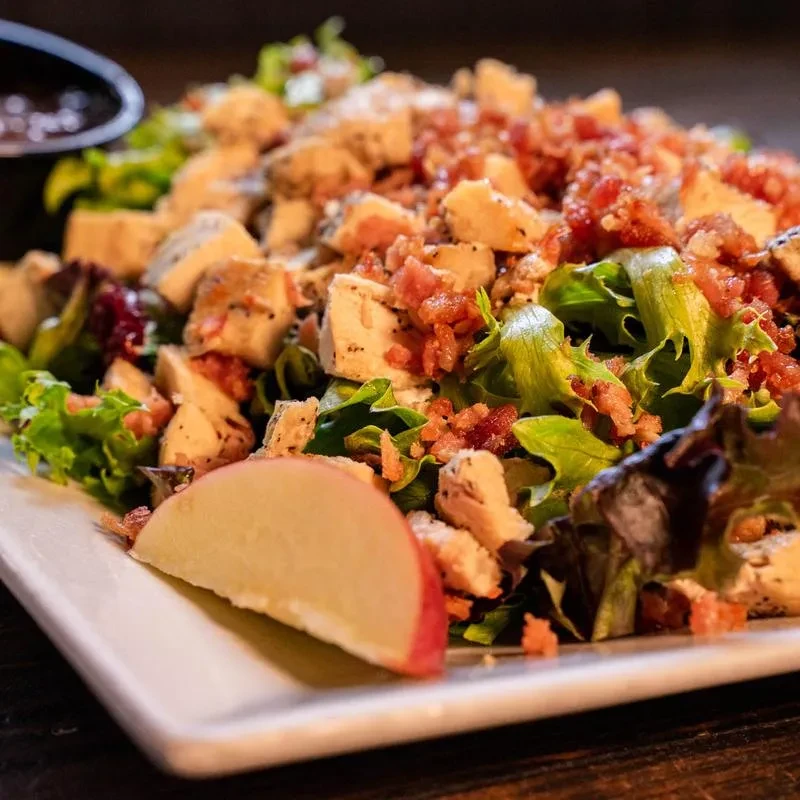Close-up of mixed greens salad with grilled chicken, bacon, and apple.