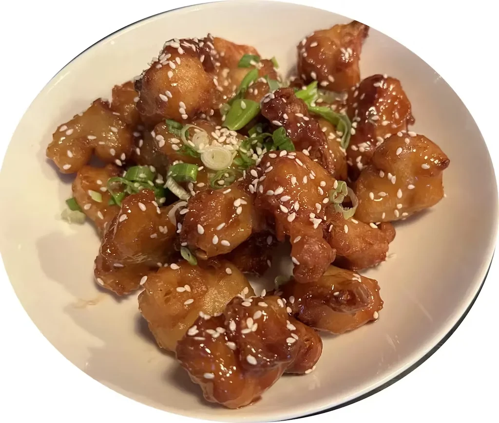 Glossy glazed fried pieces garnished with sesame and green onions.
