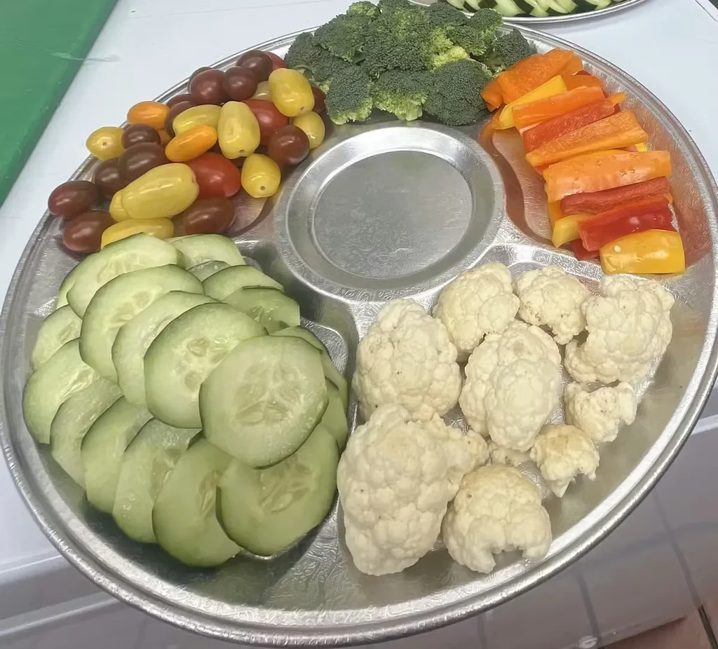 Round silver segmented platter with fresh raw vegetables and a central dip well.