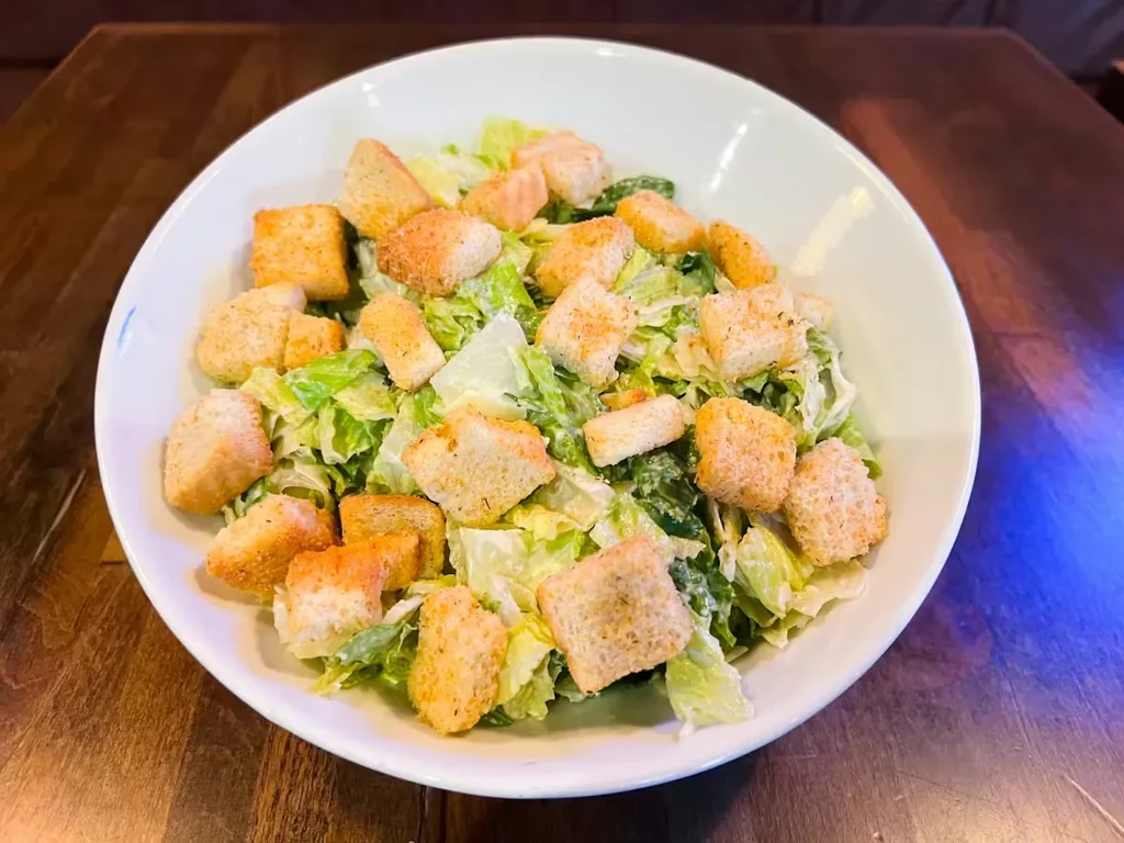 Close-up overhead of Caesar salad with romaine, croutons, and dressing.