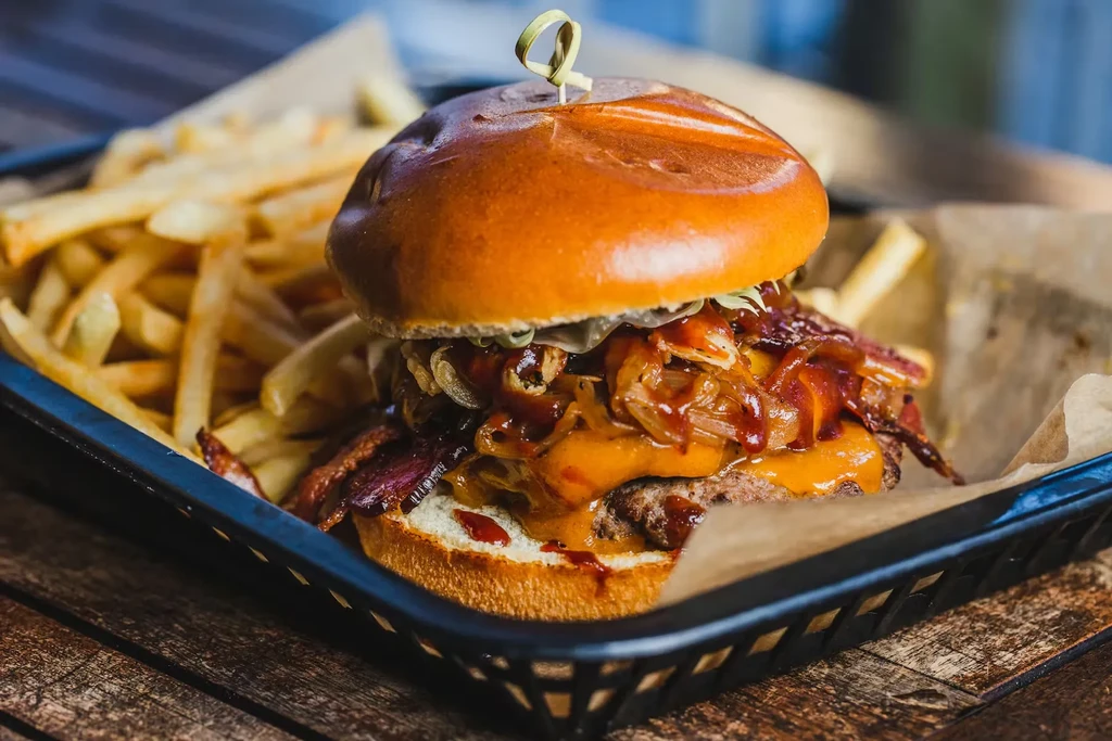 Burger with bacon, melted cheese, and golden fries in a basket.