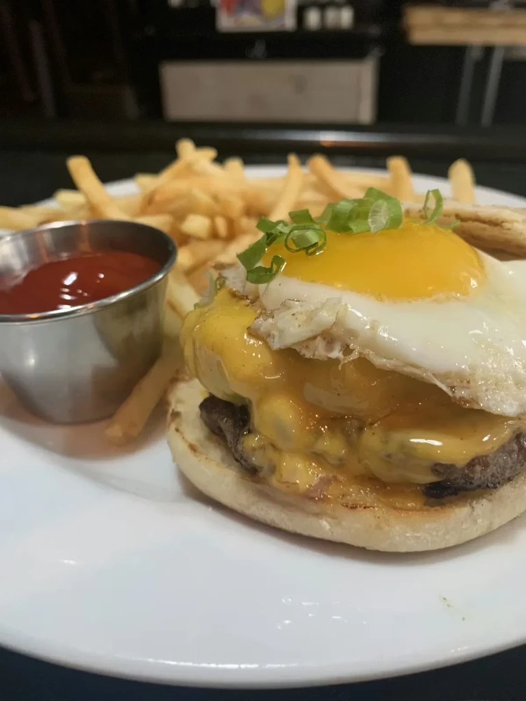 Plate with breakfast sandwich, fried egg, melted cheese, fries, and ketchup.